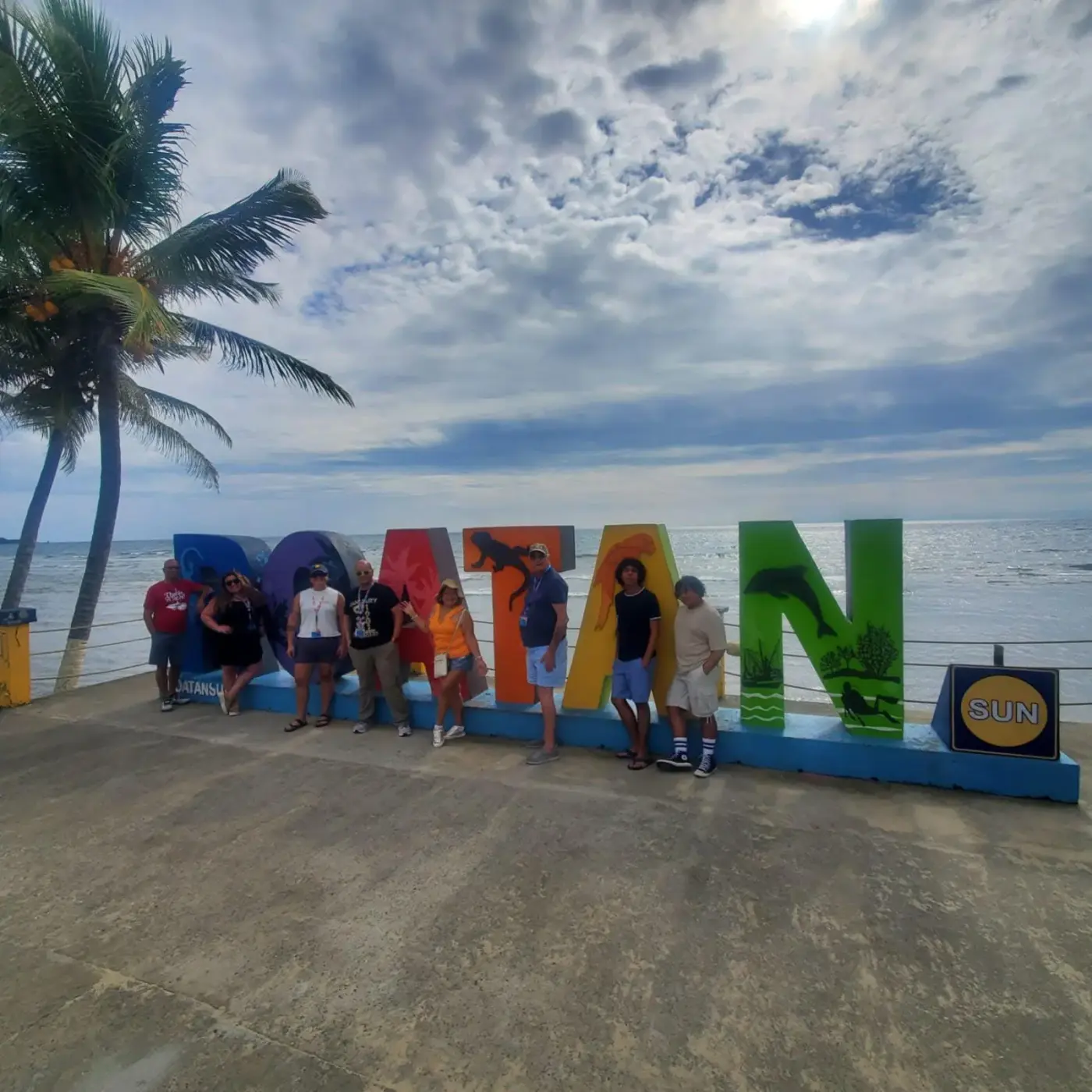 Tourists posing at colorful Roatán landmark sign by the ocean